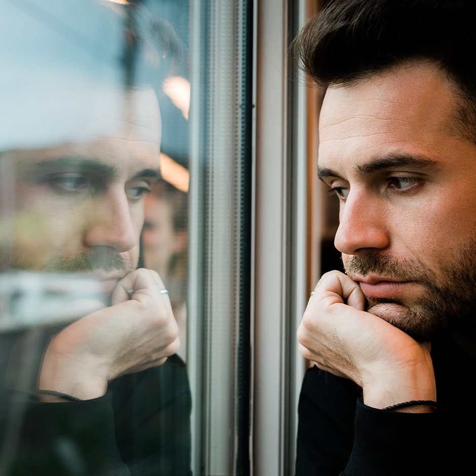 A man looking out of a window at his reflection.